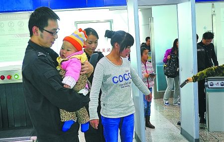 重慶江北機(jī)場(chǎng)安檢門通道工作員抱小孩兒助乘客安檢[圖]
